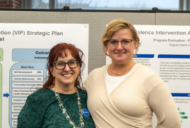 Two caucasian women smiling in front of research poster